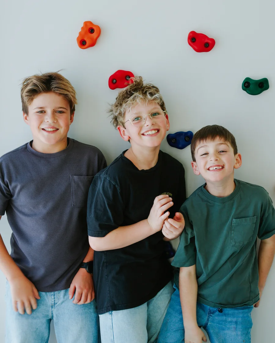 Trois enfants souriants devant le mur d'escalade de la clinique