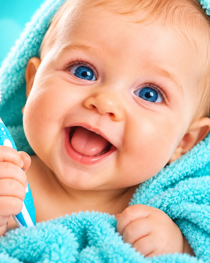 Bébé souriant dans une serviette turquoise, qui tient sa brosse à dents — Go Dentiste, dentiste pour bébé à Valleyfield et Vaudreuil-Dorion